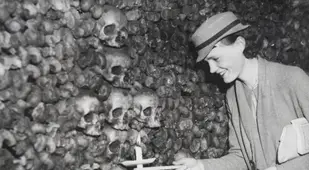 Woman holds a candle next to skulls in the Paris Catacombs