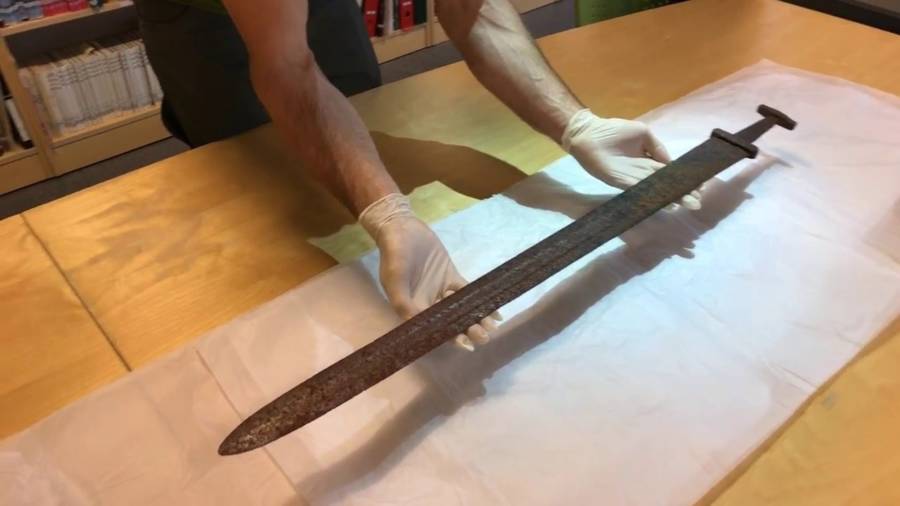  An archaeologist wearing white gloves holds a rusty Viking sword discovered in Suldal, Norway.