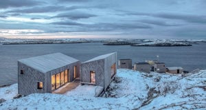 Lit Cabins In Snow By Water Featured